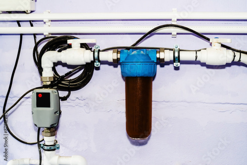 A close-up shot of a water filter system attached to a white wall. The filter is blue and white and has a brown filter cartridge