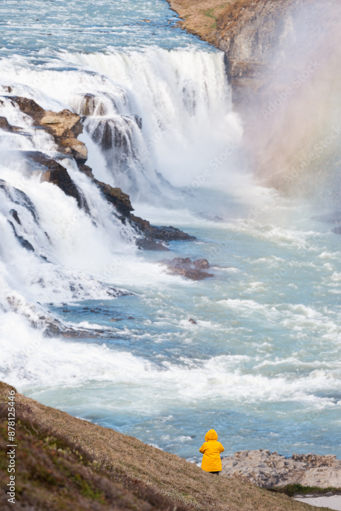 Stunning view of the Gullfoss waterfall with a tourist wearing a yellow jacket. Gullfoss is the most popular waterfall in Iceland and one of its most iconic sights.