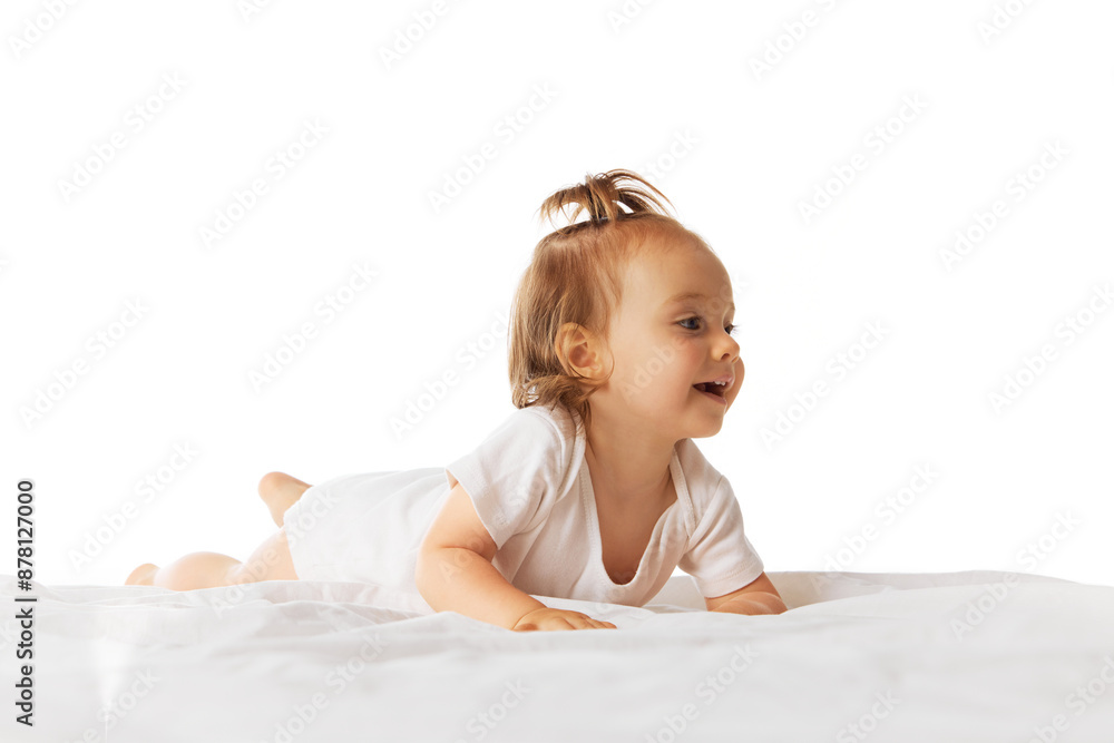 Fototapeta premium Happy little baby girl, child in bodysuit ling on belly in bed and making moves, crawling isolated on white background. Concept of childhood, care, health, infancy, lifestyle, motherhood
