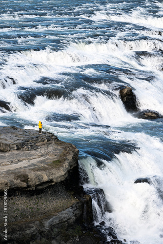 Stunning view of the Gullfoss waterfall with a tourist wearing a yellow jacket. Gullfoss is the most popular waterfall in Iceland and one of its most iconic sights.