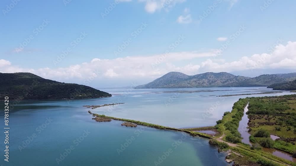 Aerial view of the serene Albanian landscape near Butrint National Archaeological Park, featuring calm blue waters, lush greenery, and distant mountains. Aerial view of the serene Albanian landscape near Butrint National Archaeological Park, featuring calm blue waters, lush greenery, and distant mountains.