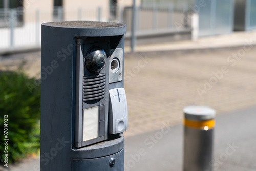 A security system with a camera, intercom, and keycard reader is mounted on a pillar outside of a building entrance. photo