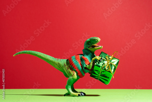 Cute dinosaur in knitted sweater with present box on red and green background. photo