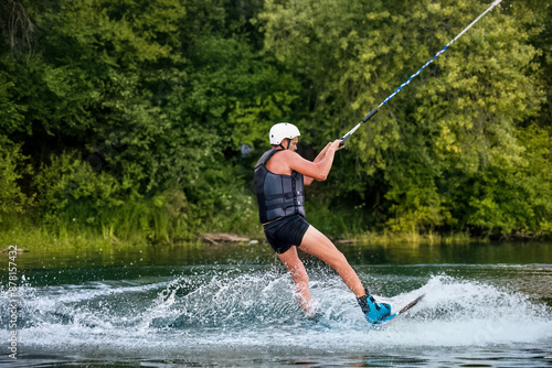 A man wakeboarding on a lake on summer day in a life jacket. Soft focus. Action blur.