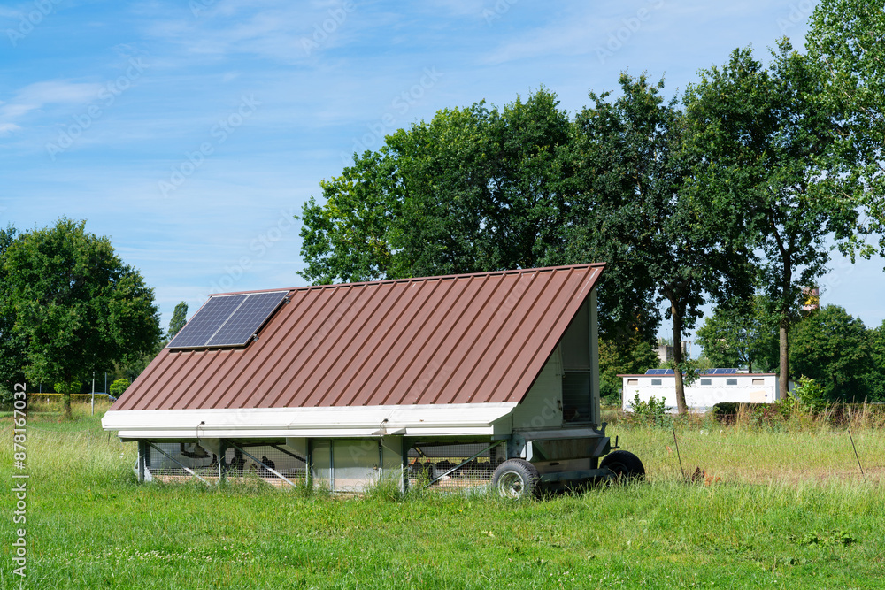 A modern, solar-powered chicken coop sits on a grassy field with trees in the background. A modern, solar-powered chicken coop sits on a grassy field with trees in the background.