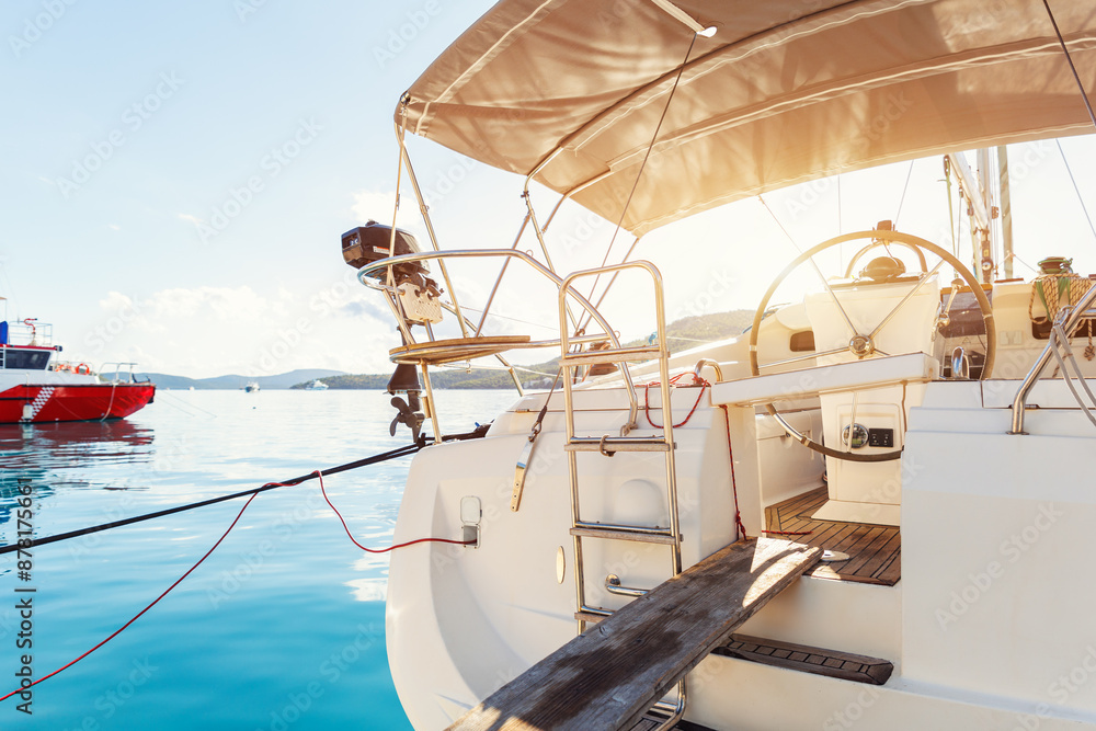 Fototapeta premium Back view modern luxury sailboat in turquoise sea ocean water marina bay harbor. Sail boat rental charter berth docking service. Nautical adventure travel lifestyle. Cruise trip vacation