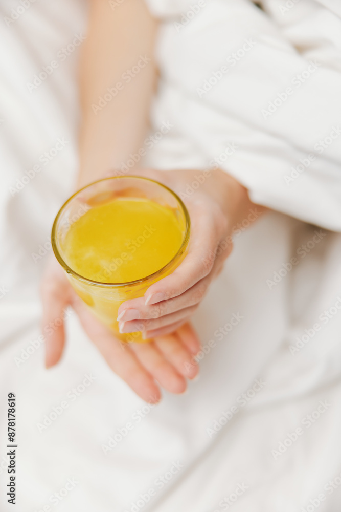 Person holding glass of orange juice while laying in bed Person holding glass of orange juice while laying in bed