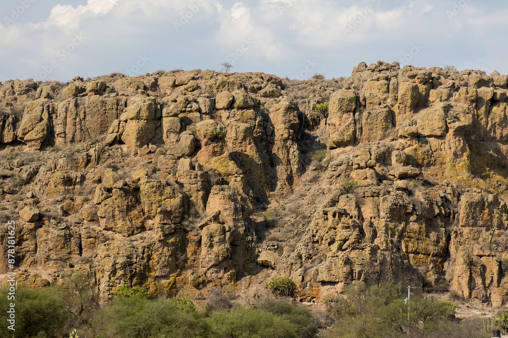 Fototapeta premium Impressive Rocky Cliff Formation Under a Partly Cloudy Sky with Verdant Vegetation Below