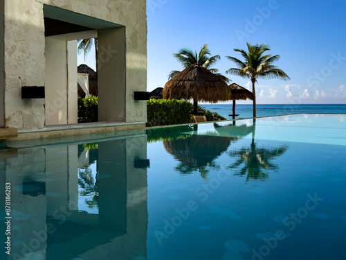 Relaxing pool of a luxury resort hotel, with a beach of fine white and golden Caribbean sand, bathed by crystal clear turquoise water in the background, ideal place for vacation and relaxation. photo