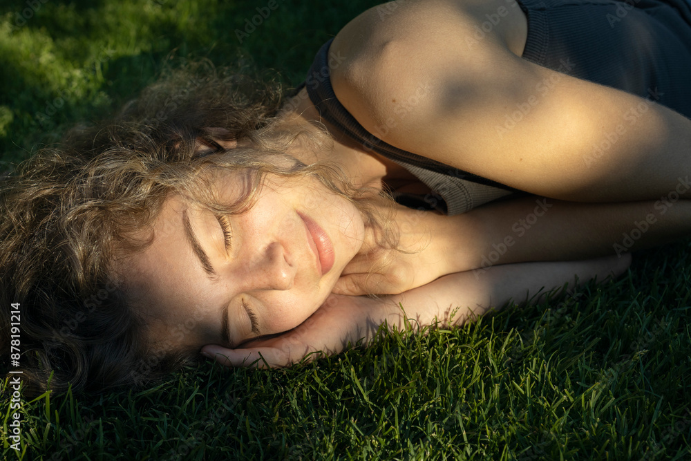 close-up of face of beautiful teenage girl lying with eyes closed on grass under rays of sunlight. enjoying nature outdoors. Young woman relaxes, daydreaming in park. Spring, summer, sunbathing close-up of face of beautiful teenage girl lying with eyes closed on grass under rays of sunlight. enjoying nature outdoors. Young woman relaxes, daydreaming in park. Spring, summer, sunbathing
