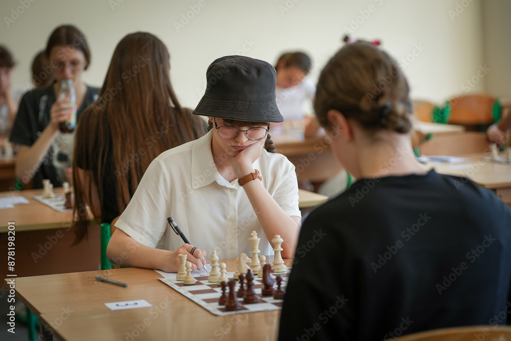 Naklejka premium The girl plays chess in club, leisure activity of weekend and compitetion concept. Pieces on the chessboard. Chess game, close-up, portrait. Chess tournament, competition