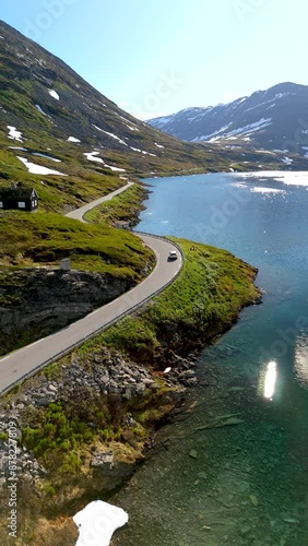 A winding road alongside a beautiful, clear lake surrounded by mountains. Snow still covers the peaks. Langvatnet, Geiranger, Norway photo