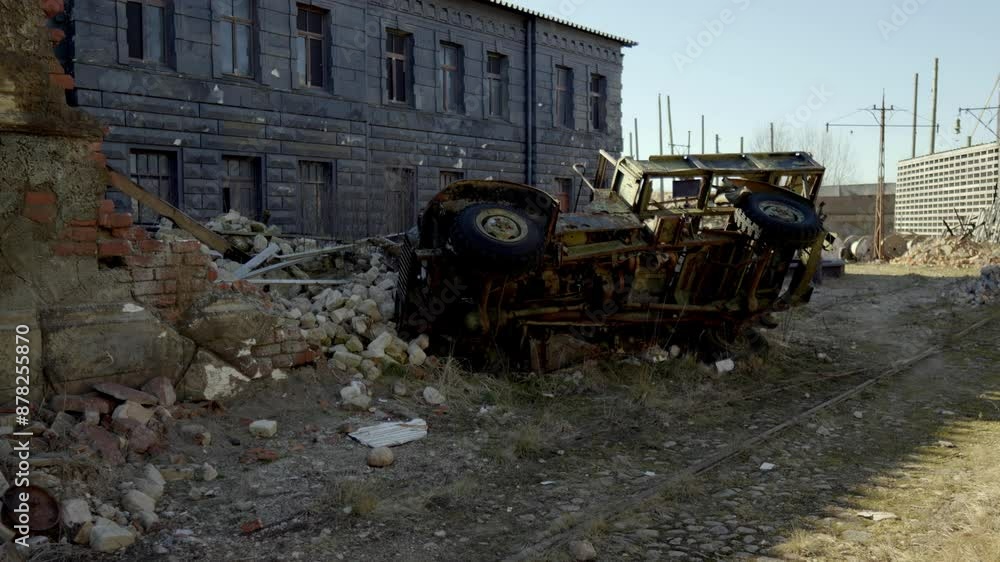 Cinevilla car is upside down in a field next to a building. The car is old and rusted