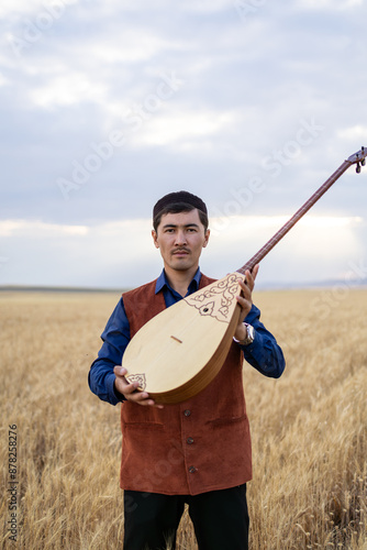 Kazakh, a man in Kazakh national dress playing dombra in the steppe. Kazakhstan. Central Asia. Nomads. | Казах, мужчина в казахской национальной одежде играет на домбре в степи. Казахстан.Средняя Азия photo