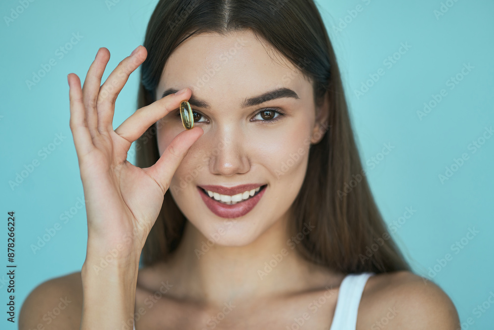 Woman Holding Omega-3 Against Eye, Smiling Against Blue Background. Concept Of Engagement, Happiness, And Love. Woman Holding Omega-3 Against Eye, Smiling Against Blue Background. Concept Of Engagement, Happiness, And Love.
