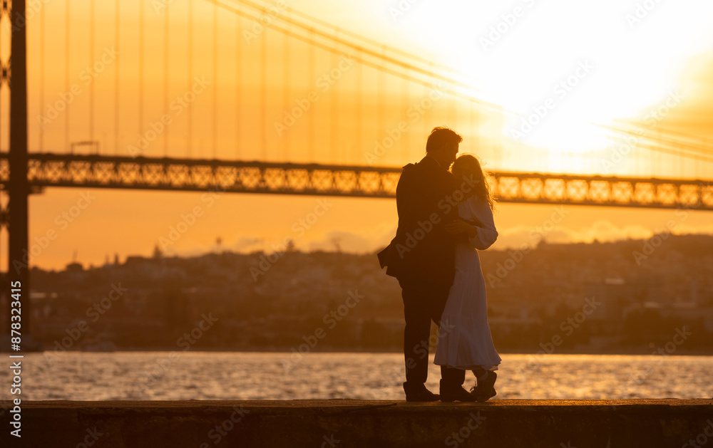 Fototapeta premium A couple is kissing in front of a bridge with the sun setting in the background
