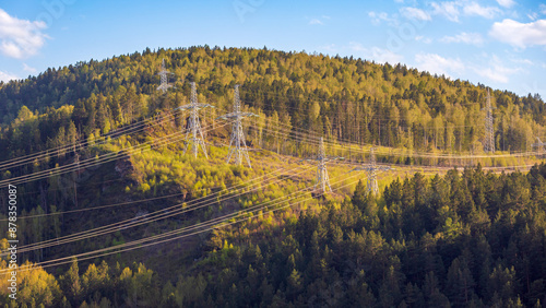 Fotografie Power lines pylons with electric wires in mountainous area covered with coniferous forest