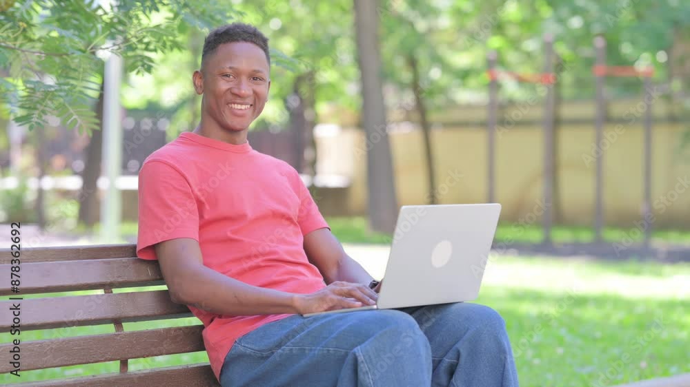 Casual African Man Smiling at Camera with Laptop in Lap Outdoor Casual African Man Smiling at Camera with Laptop in Lap Outdoor
