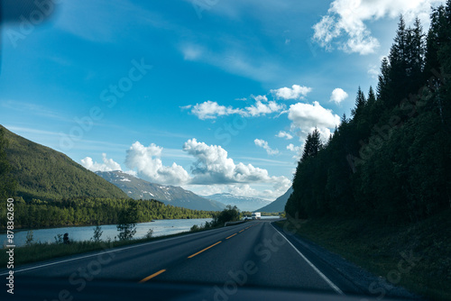 A river next to a country road with mountains on each side from the view of a car dashboard