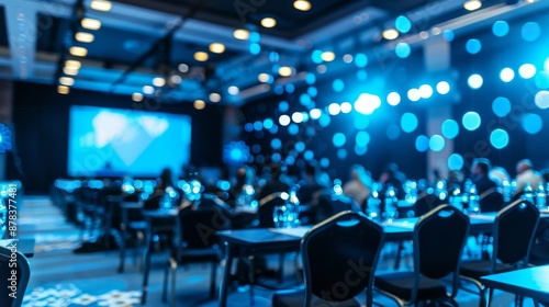 A large conference hall with blue lights and a screen at the front. There are chairs set up for the audience.