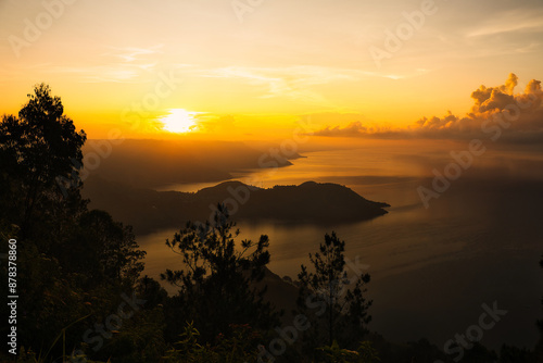 This captivating photo captures a golden sunrise over Lake Toba in Sumatra, Indonesia. The serene waters and lush hills create a tranquil scene, perfect for nature and travel enthusiasts seeking a bre photo