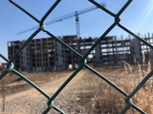 Incomplete construction of a residential high-rise building, apartment house behind metal fence. Crisis in construction business. Construction crane.