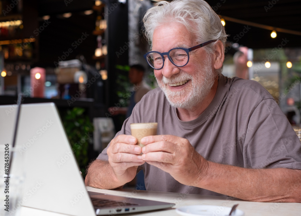 An elderly man enjoying a coffee and pastry in a cafe, smiles while using his laptop on a video call. Cheerful senior male, highlighting happiness and contentment in a relaxed atmosphere An elderly man enjoying a coffee and pastry in a cafe, smiles while using his laptop on a video call. Cheerful senior male, highlighting happiness and contentment in a relaxed atmosphere