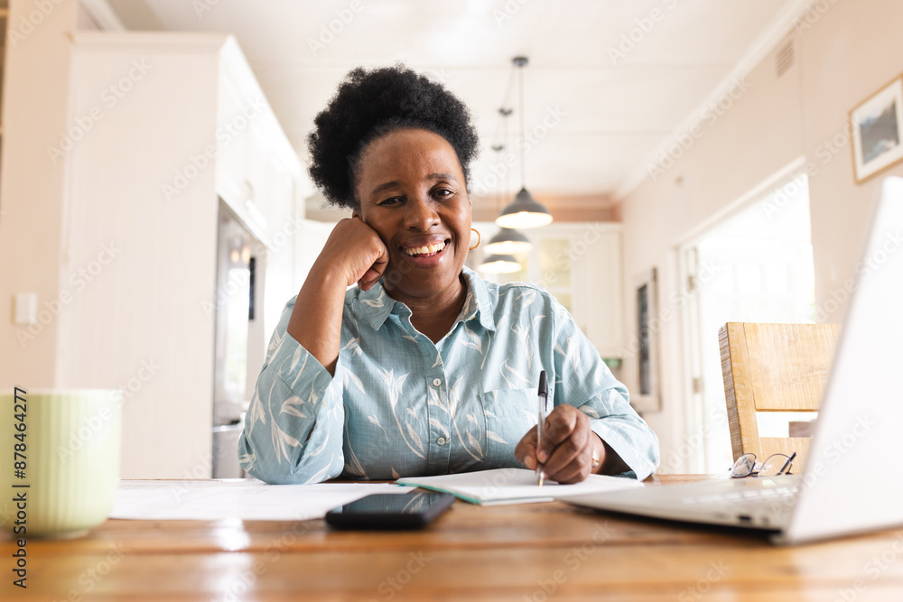 Portrait of happy senior african american woman with documents on table using laptop at home Portrait of happy senior african american woman with documents on table using laptop at home