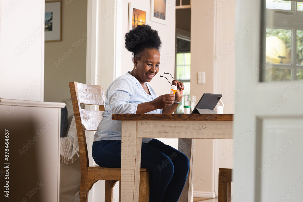 Happy senior african american woman holding pills and using tablet at home Happy senior african american woman holding pills and using tablet at home