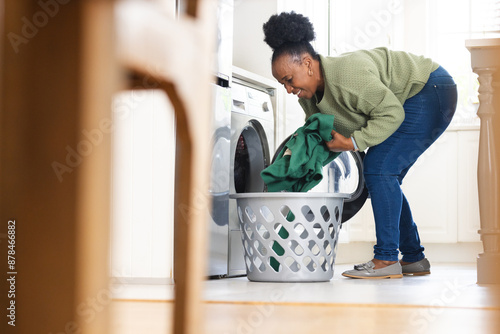 Happy senior african american woman doing laundry in kitchen at home
