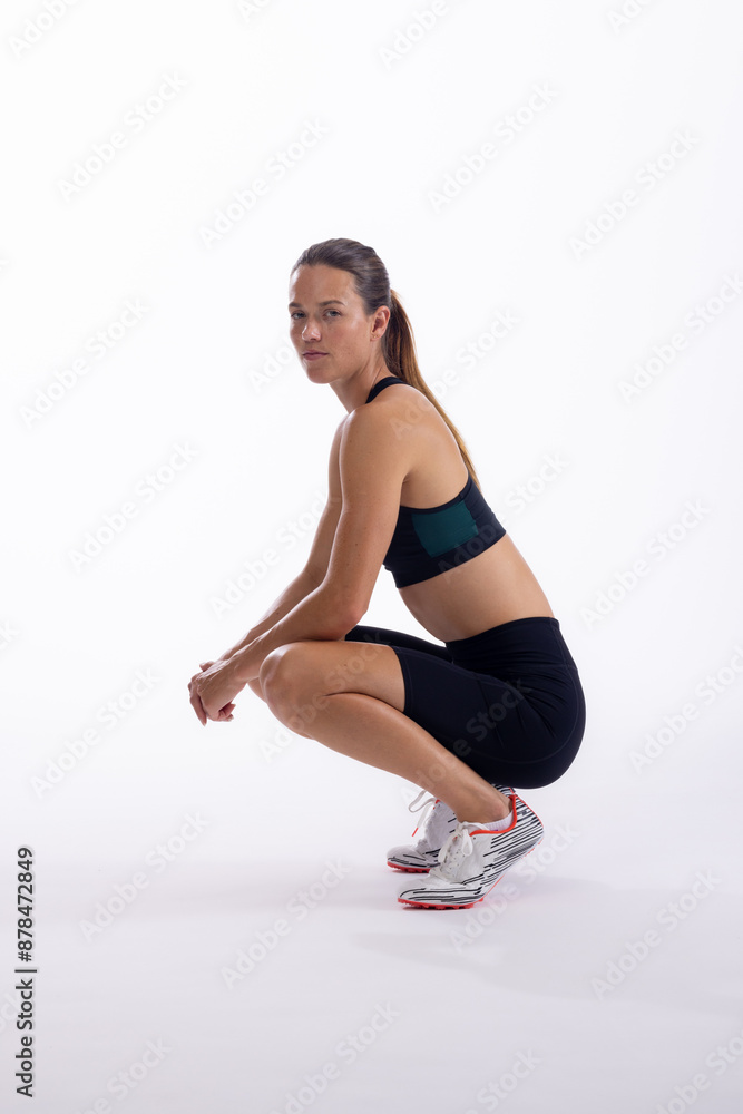 Young Caucasian female athlete performs a squat exercise on a white background Young Caucasian female athlete performs a squat exercise on a white background