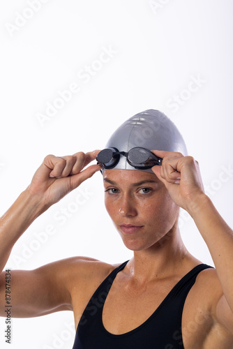 Young Caucasian female swimmer adjusts her swimming goggles on a white background, with copy space