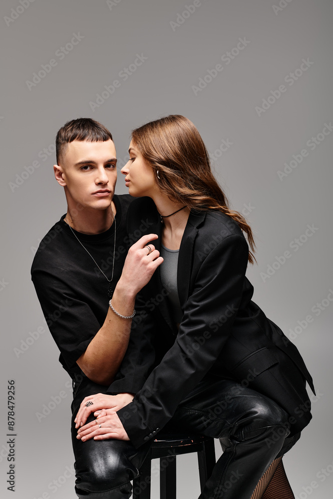 A young man and woman sitting closely together on a stool in a studio with a grey background. A young man and woman sitting closely together on a stool in a studio with a grey background.