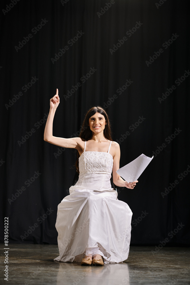 Fototapeta premium Elegant woman in white dress sits gracefully on stage during rehearsals.