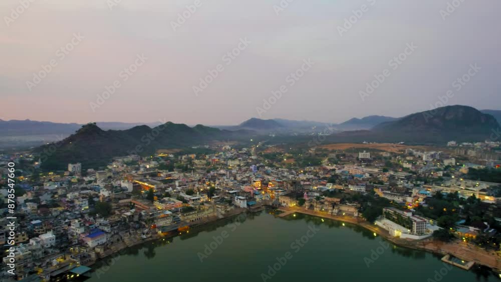 Aerial drone panning shot over hindu holy city of pushkar with lake bhrama temple visible in city lights and aravalli hills covered in fog in distance showing cityscape in Rajasthan India Aerial drone panning shot over hindu holy city of pushkar with lake bhrama temple visible in city lights and aravalli hills covered in fog in distance showing cityscape in Rajasthan India