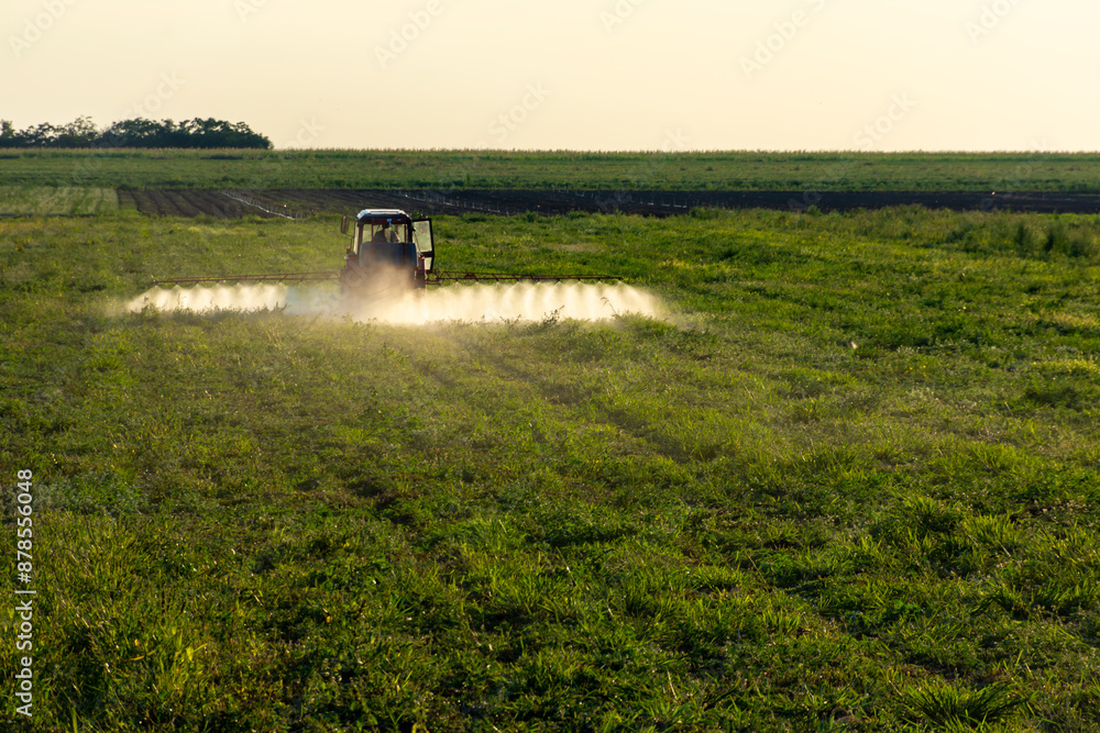 Fototapeta premium A tractor spraying a field with fertilizer, surrounded by trees and land