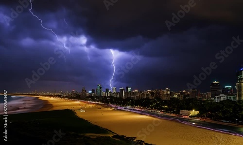 Lightning with thunderstorm clouds at night at night over cityscape on beach.
