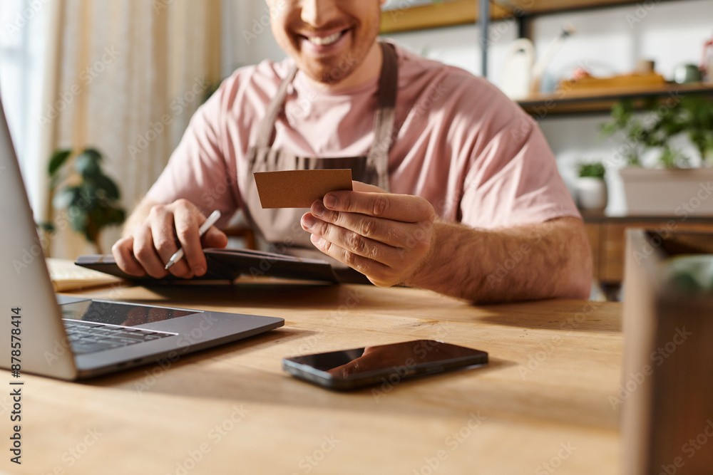 A man sitting at a table with a laptop and a credit card, making an online purchase for his small business. A man sitting at a table with a laptop and a credit card, making an online purchase for his small business.