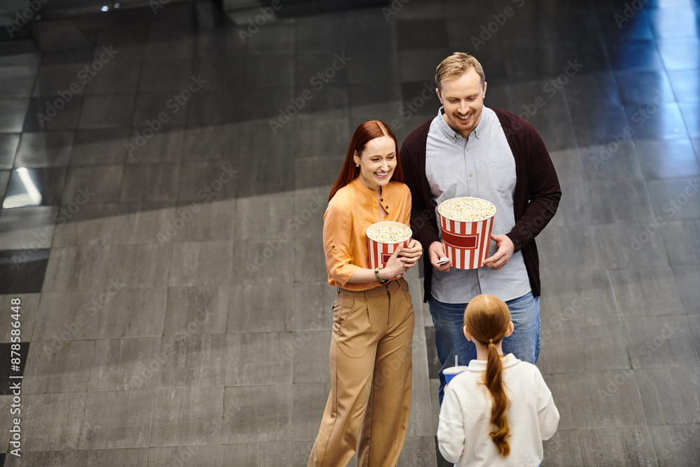 Obraz premium A happy family at the cinema, holding a bucket of popcorn and enjoying a movie together.