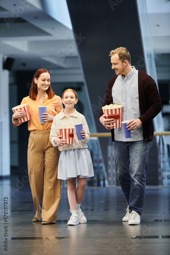 A man, woman, and child joyfully hold popcorn boxes as they spend quality time together at the cinema. photo