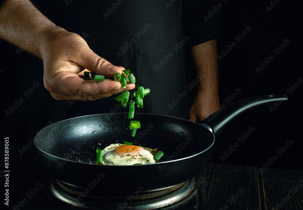 Chef adds chopped green onion to the pan with eggs by hand. Concept of cooking healthy food with egg in hotel kitchen.