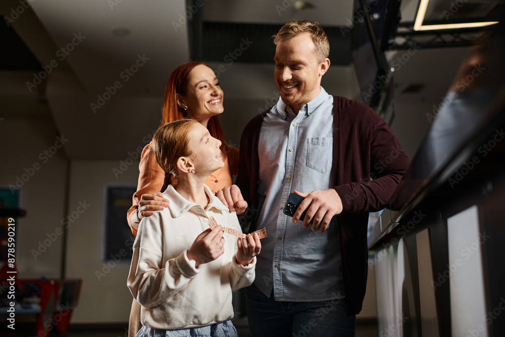 A man and a woman stand together with daughter, embodying unity and love, enjoying a special moment at the cinema as a happy family. A man and a woman stand together with daughter, embodying unity and love, enjoying a special moment at the cinema as a happy family.