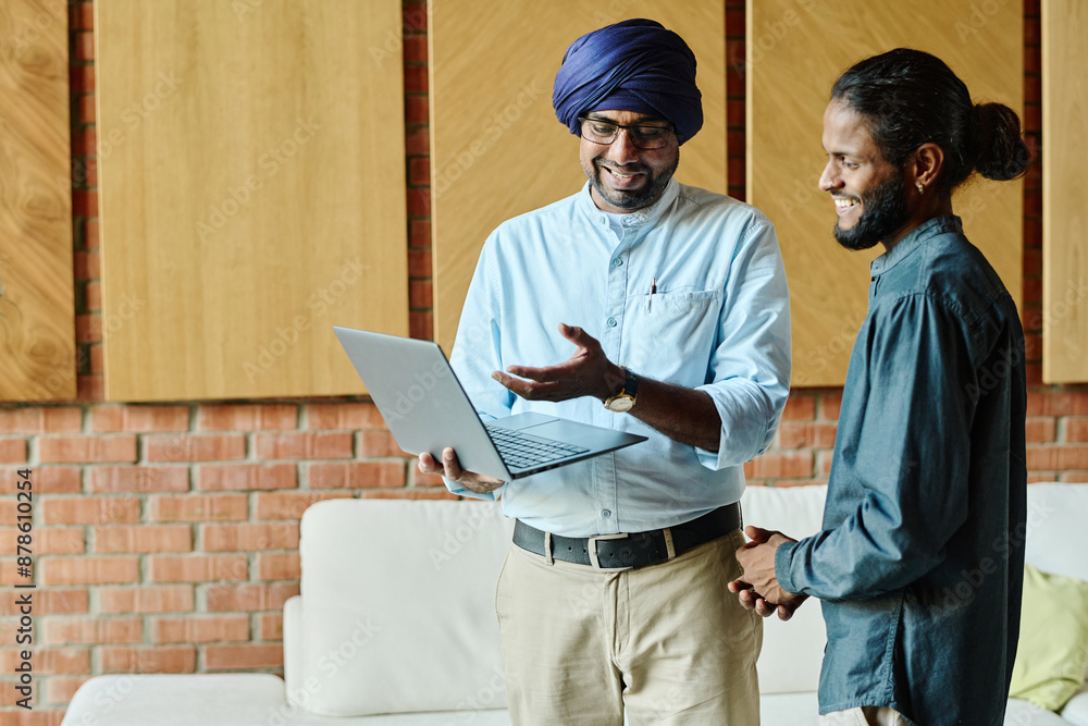 Two Indian colleagues standing in office waiting zone while one of them showing presentation, thrilled and full of enthusiasm Two Indian colleagues standing in office waiting zone while one of them showing presentation, thrilled and full of enthusiasm