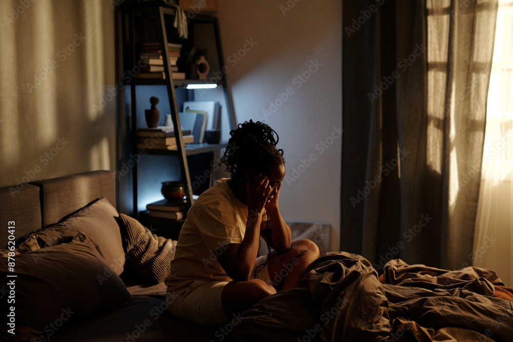 Sleepless young woman touching her temples while sitting on bed in the middle of the night and suffering from insomnia or PTSD Sleepless young woman touching her temples while sitting on bed in the middle of the night and suffering from insomnia or PTSD