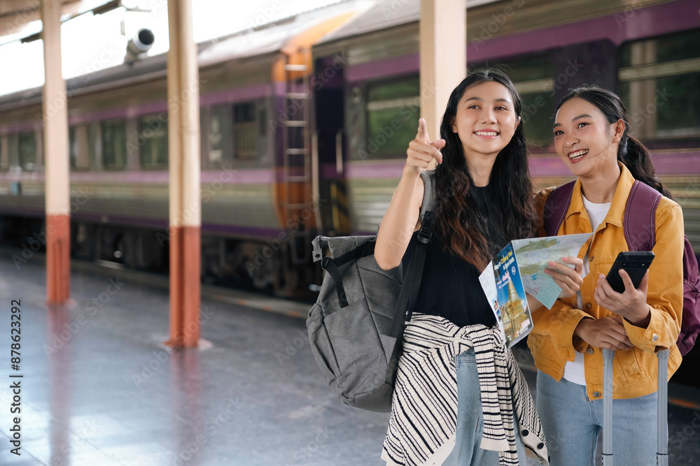 Obraz premium Two young women excitedly planning their next adventure in a bustling train station. Engrossed in a map and smartphone. Exuding wanderlust with luggage by their side