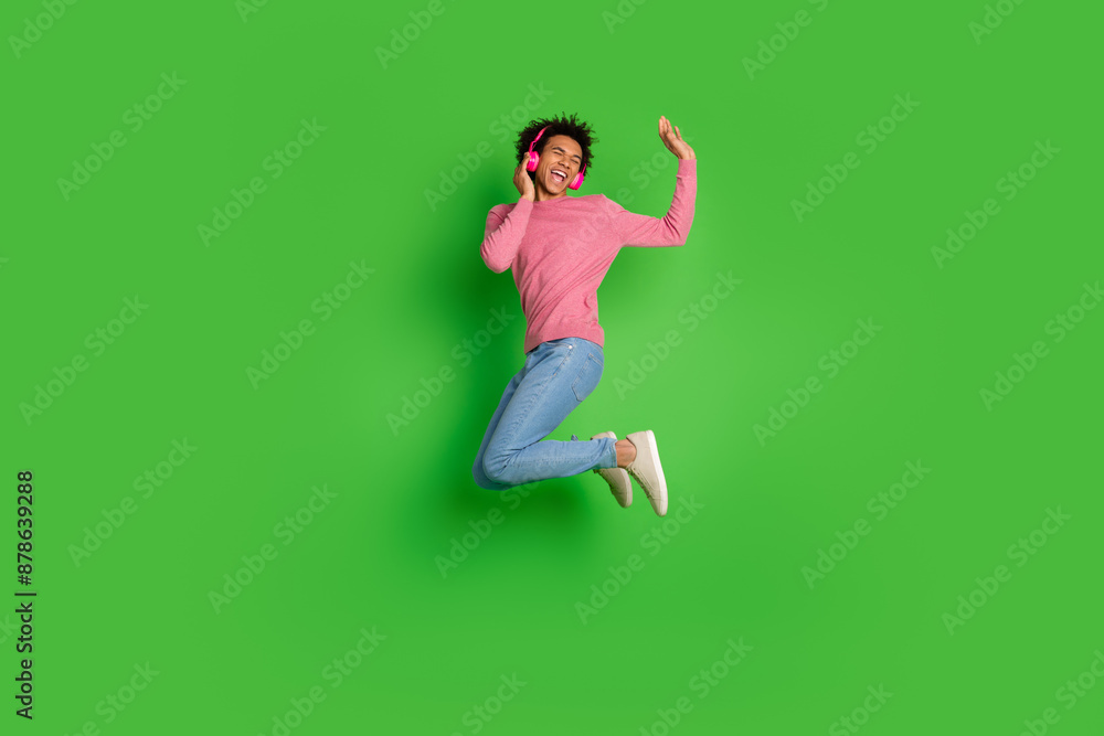 Full length photo of attractive funny guy wear pink sweater jumping high enjoy songs isolated green color background Full length photo of attractive funny guy wear pink sweater jumping high enjoy songs isolated green color background
