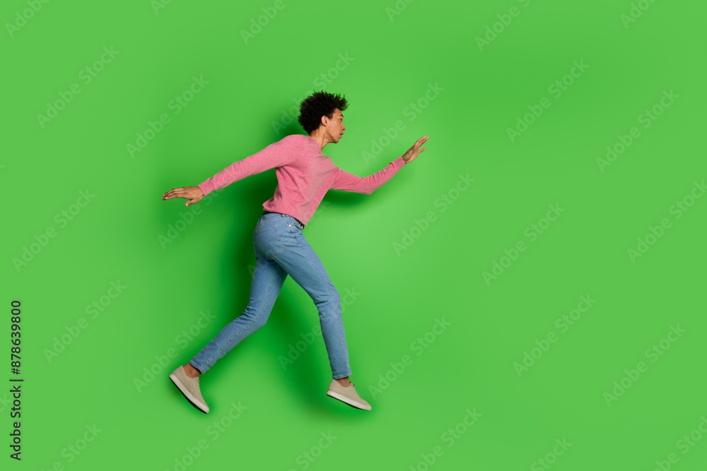 Full length photo of attractive funny guy wear pink sweater jumping high walking emtpy space isolated green color background Full length photo of attractive funny guy wear pink sweater jumping high walking emtpy space isolated green color background