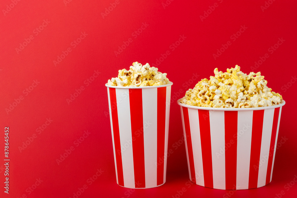 Popcorn box. Red and white striped buckets of salted popcorn on a red background. Cinema and entertainment concept. Movie night with popcorn. Delicious appetizer, snack. Place for text. Popcorn box. Red and white striped buckets of salted popcorn on a red background. Cinema and entertainment concept. Movie night with popcorn. Delicious appetizer, snack. Place for text.
