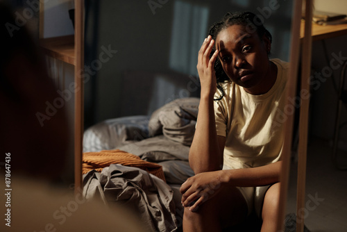 Young broken hearted and lonely woman touching her head and looking in mirror while sitting on bed at midnight during insomnia photo