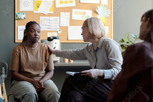 Tableau sur toile Blond mature female psychologist touching shoulder of upset African American gir